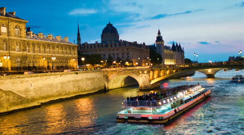 A lit Bateaux-Mouches-style cruise boat passing the Conciergerie at blue hour