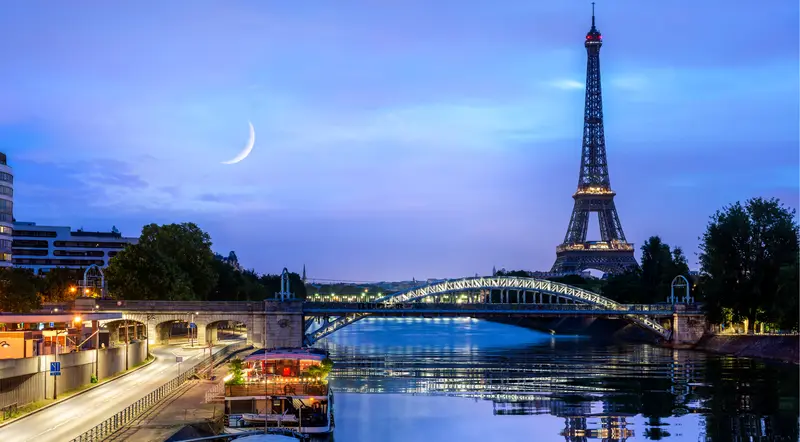 The illuminated Eiffel Tower at night with a crescent moon over the Seine