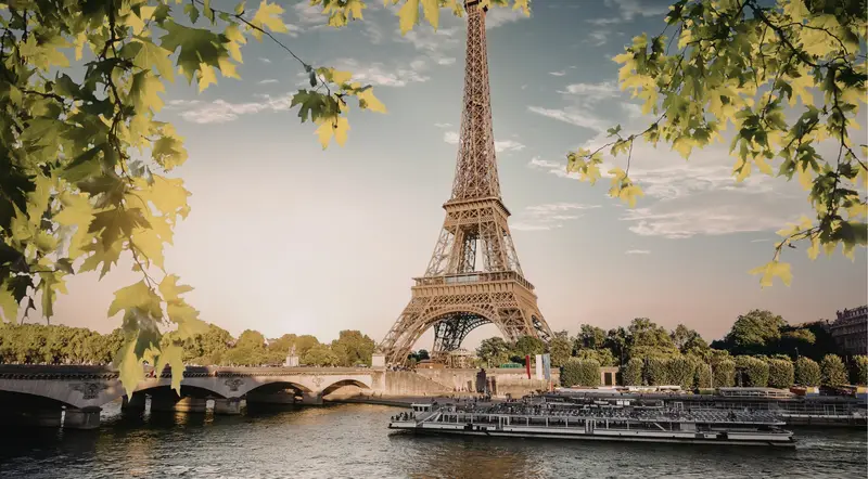 The Eiffel Tower framed by leaves above a Seine cruise boat in Paris