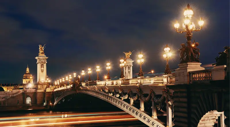 The gilded lamps and statues of Pont Alexandre III glowing at night
