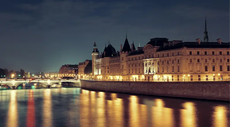 The illuminated Conciergerie reflected on the Seine at night in Paris